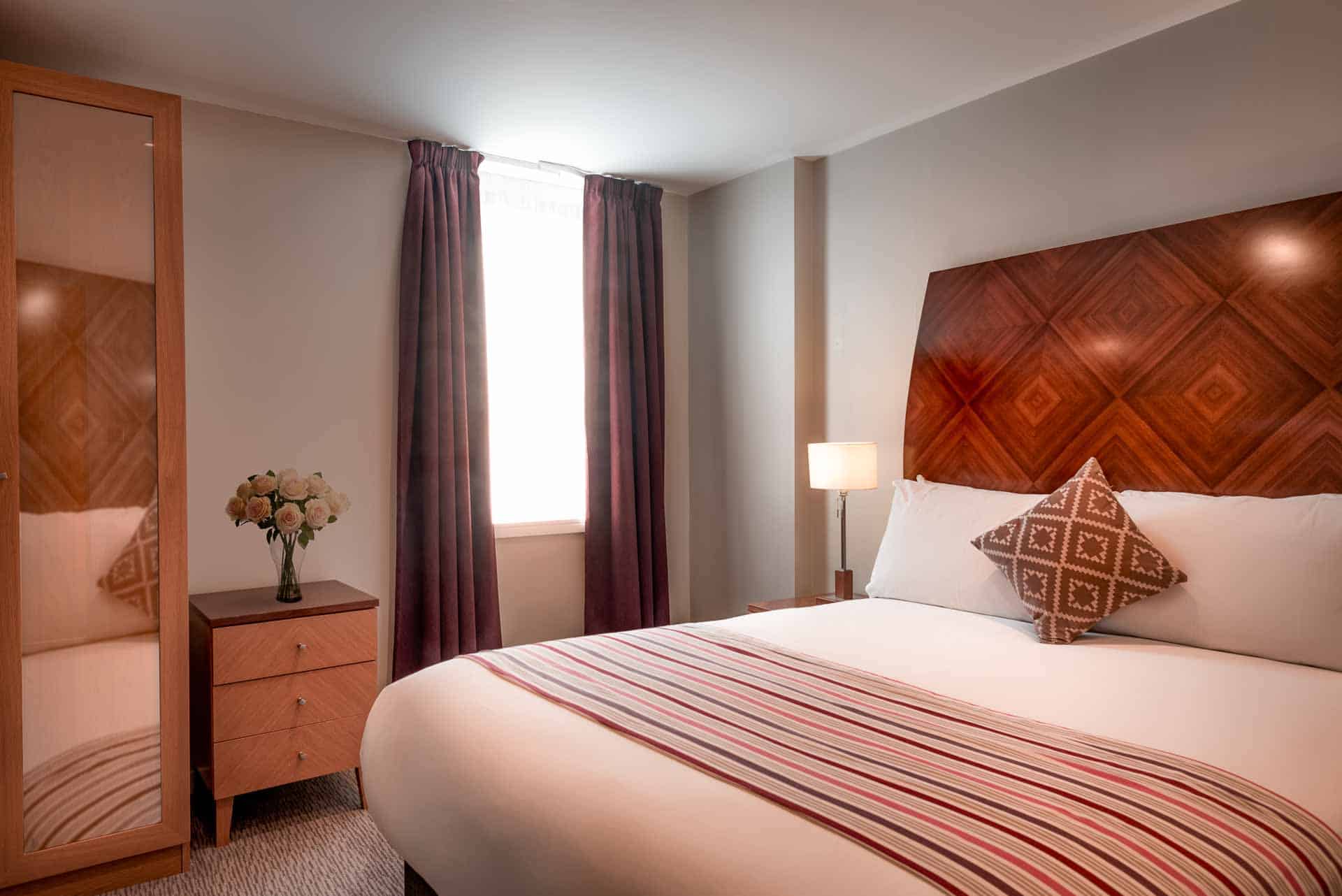 Bedroom with large bed, wardrobe and locker with natural light through window at PREMIER SUITES Manchester