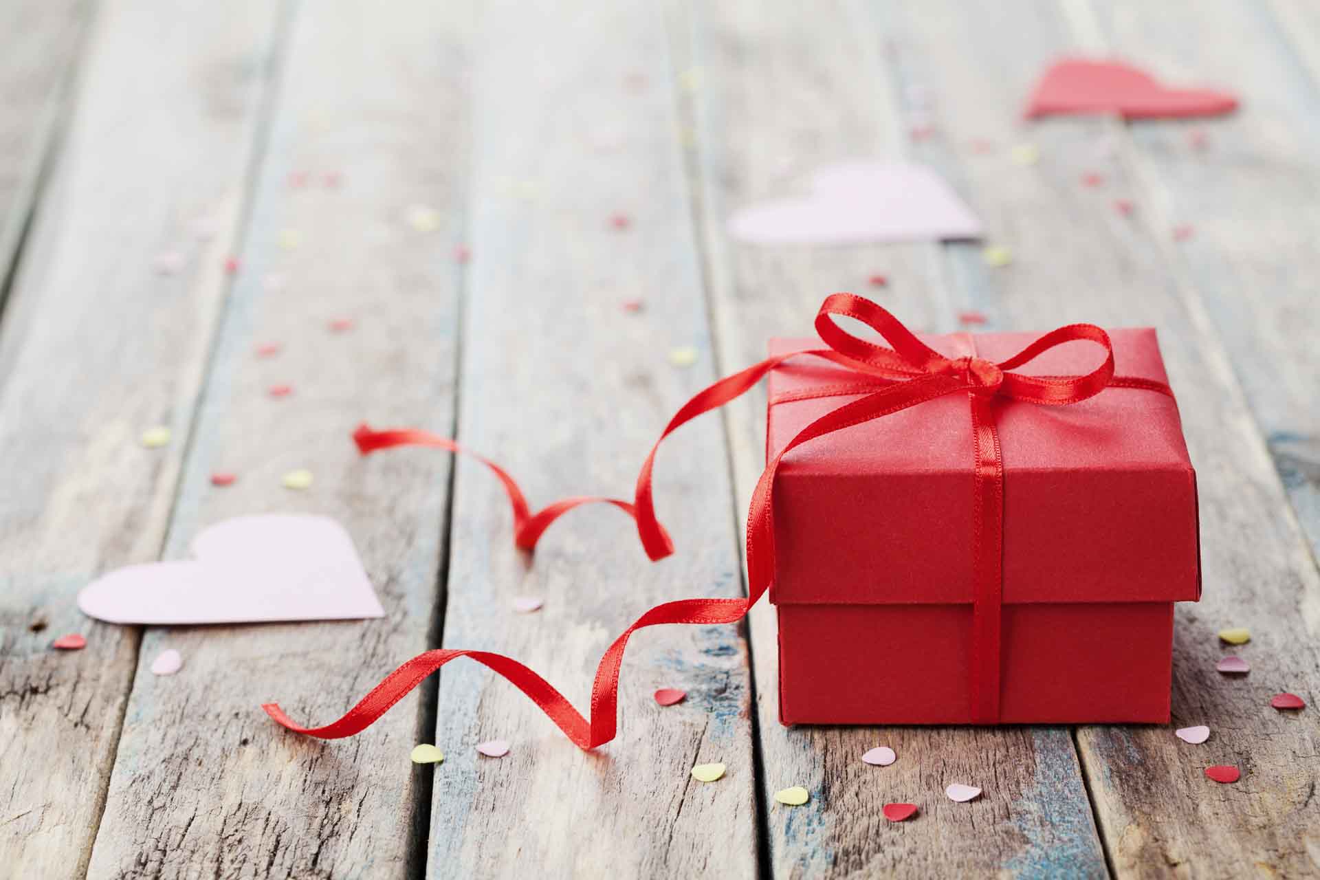 Geschenkdoos met rood striklint en papieren hart op houten tafel voor Valentijnsdag.