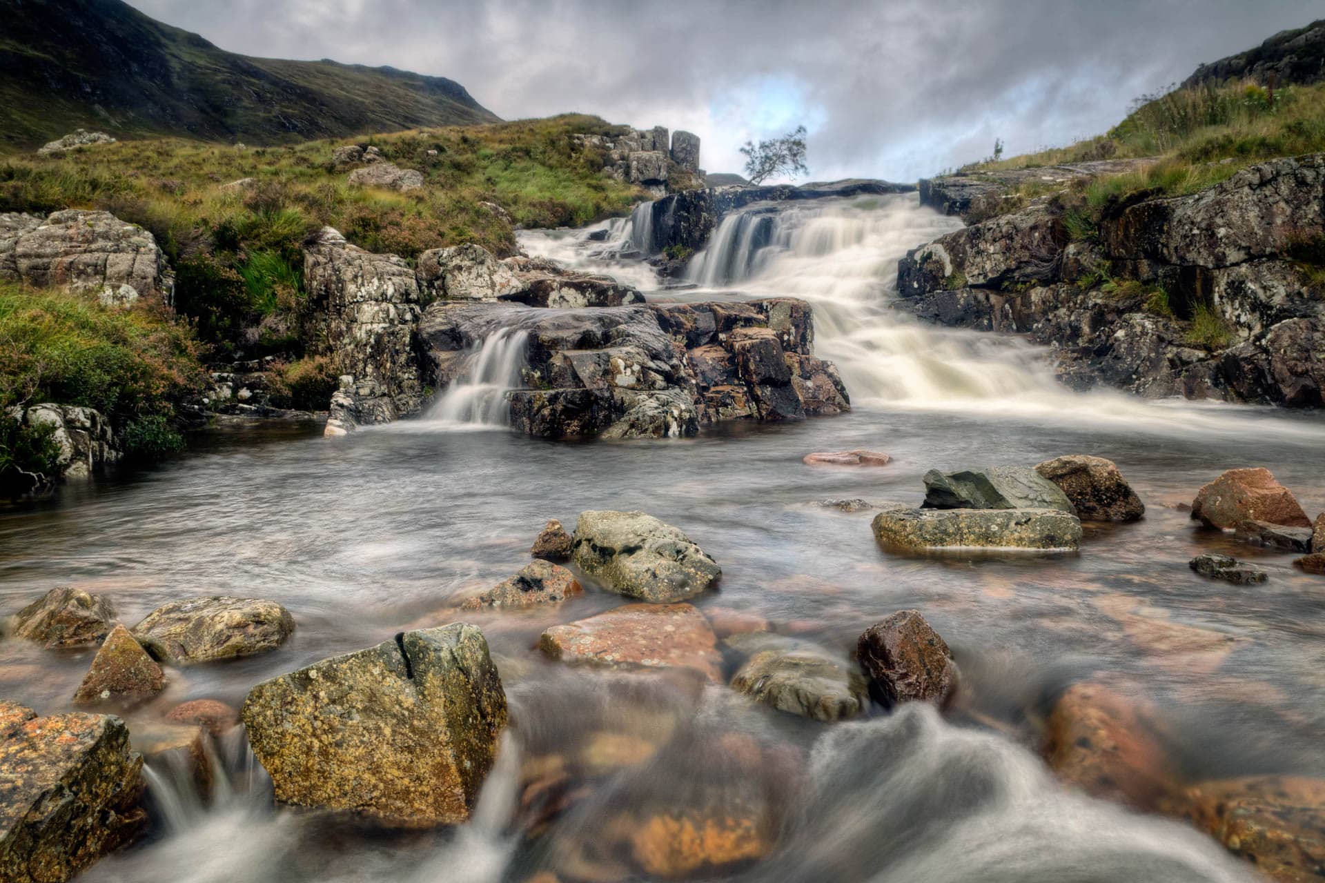 Un ruisseau dévale le flanc d'une montagne en traversant des rochers rustiques à Glen Coe, Glasgow.