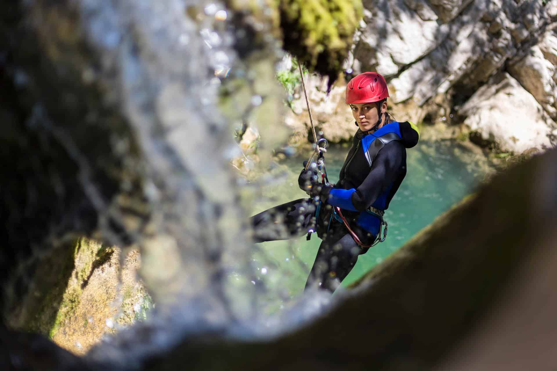 Frau beim Abseilen im Canyon Abenteuer mit Wasserfall und türkisfarbenem Wasser im Hintergrund.