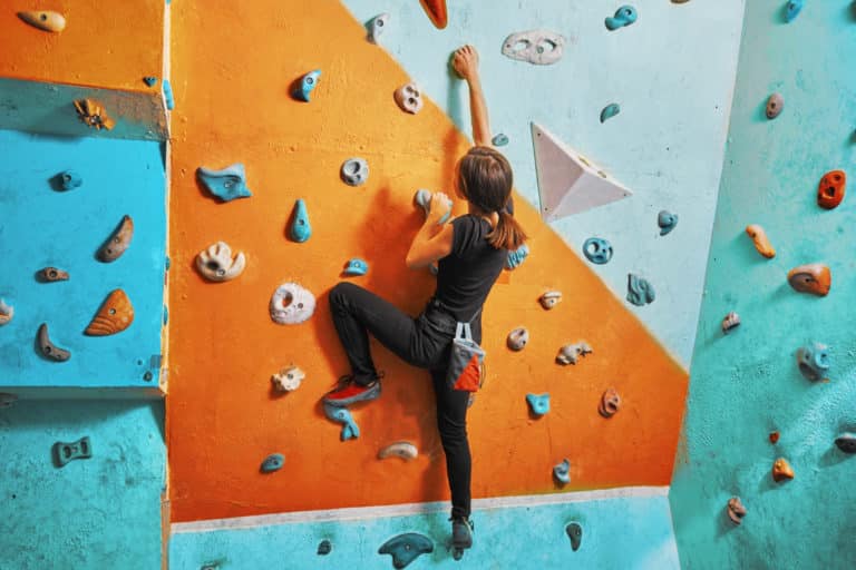 Jonge vrouw die op oefeningsmuur in gymnastiek beklimt, achteraanzicht