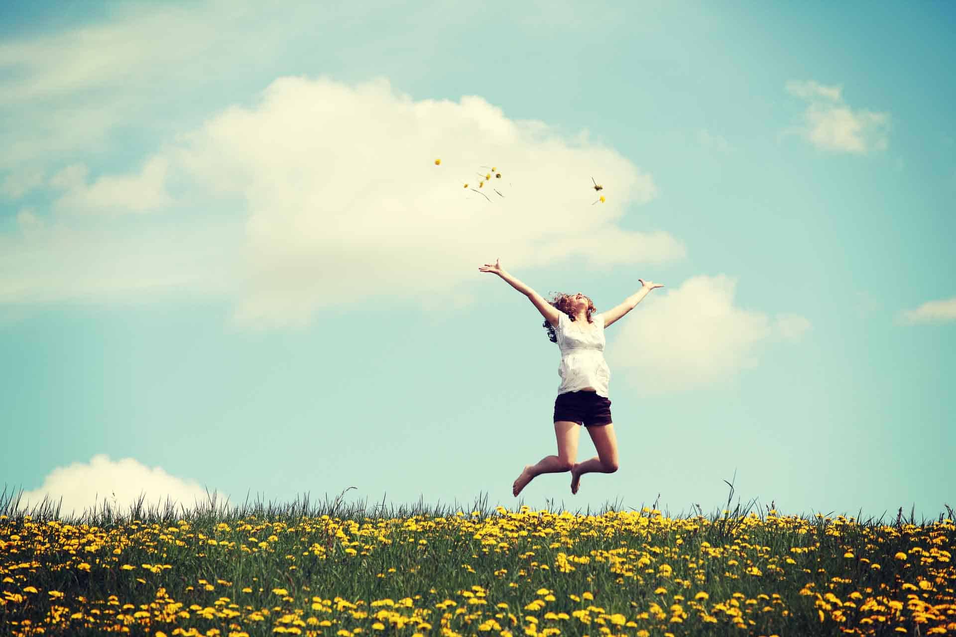 Femme heureuse sautant sur une prairie fleurie.