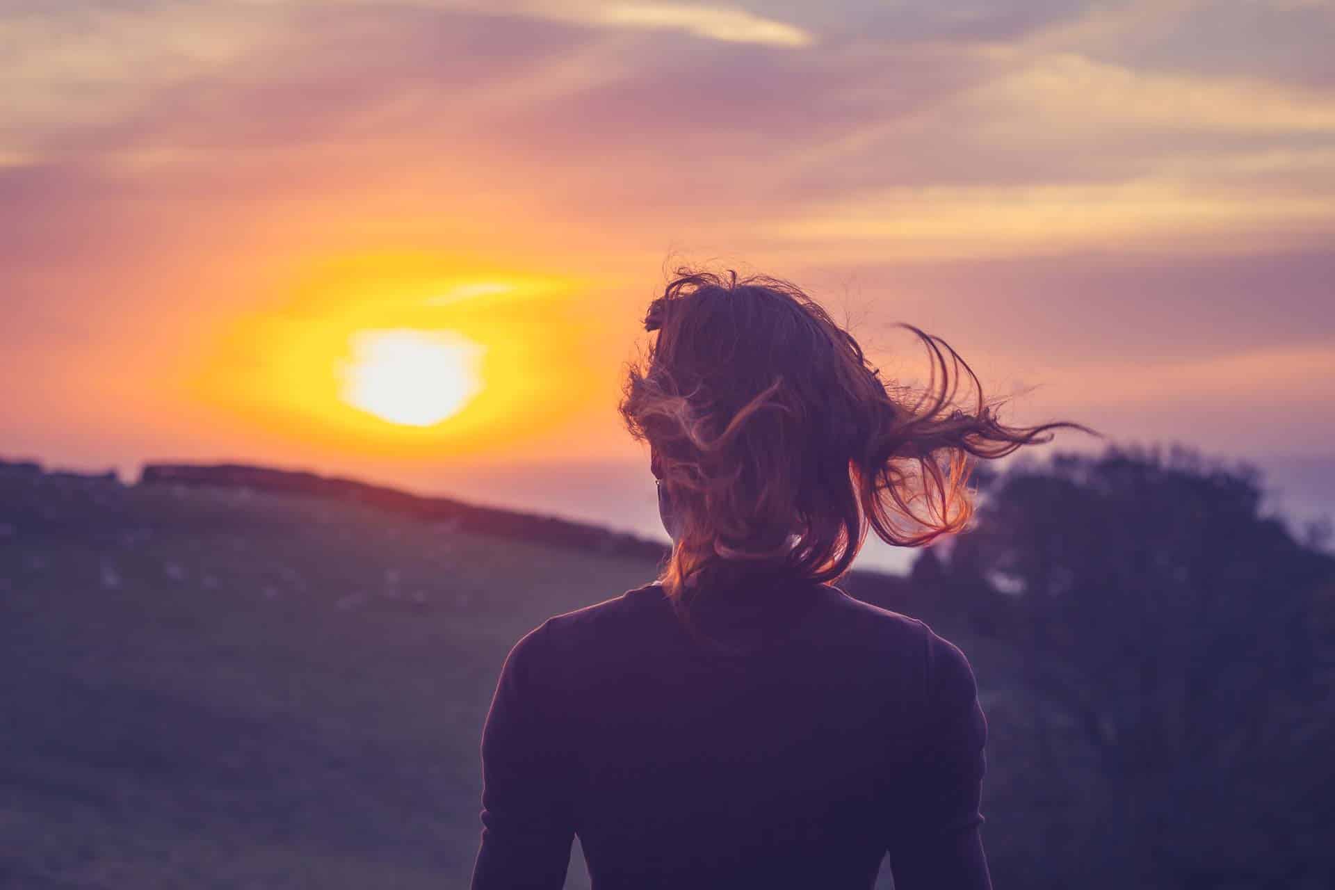 Jonge vrouw, die de zonsondergang bewondert, boven de velden.