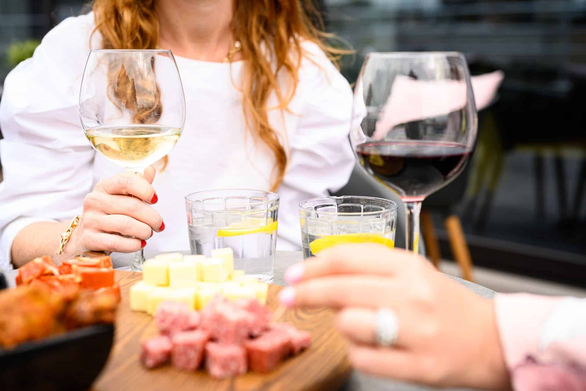 Femme aux cheveux roux tenant un verre de vin avec d'autres amuse-gueules sur la table