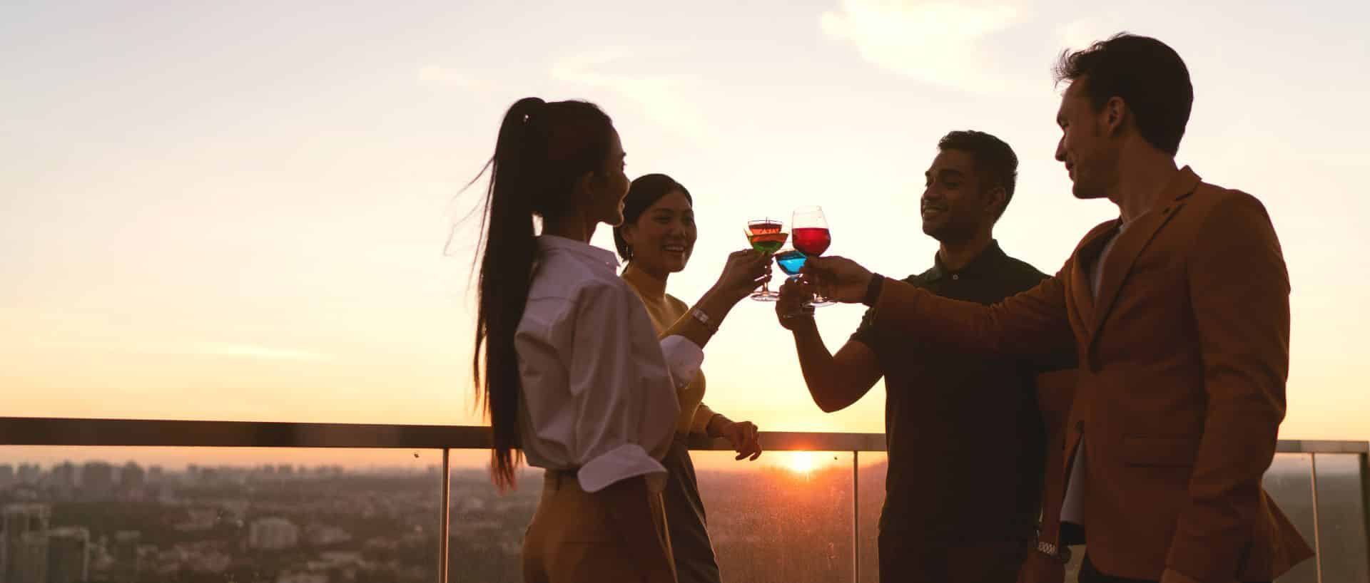 groupe de personnes sur un toit, buvant un verre ensemble au coucher du soleil
