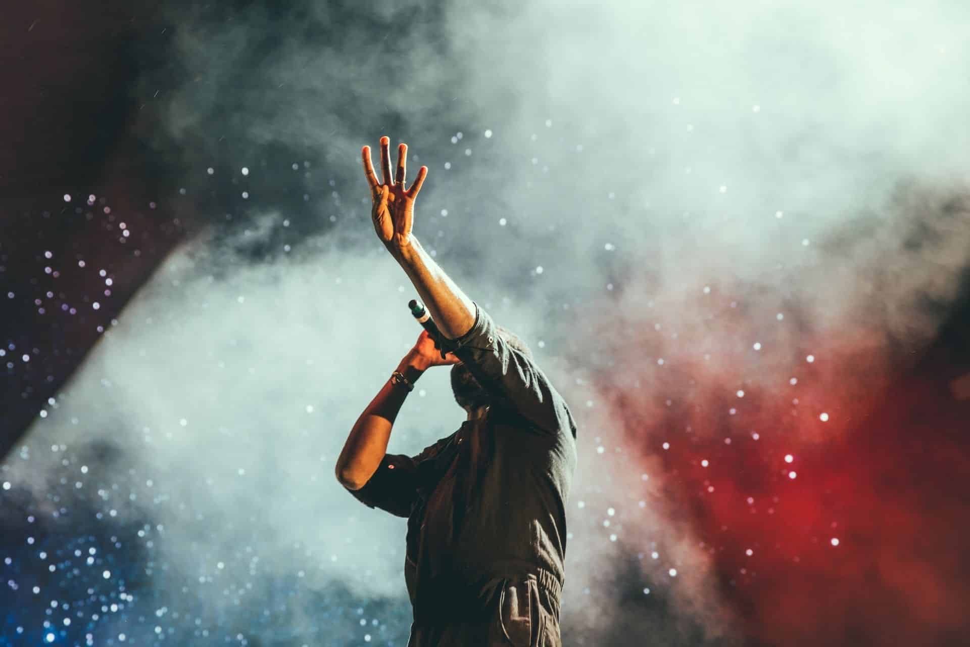 Homme levant la main tout en chantant lors d'un concert avec de la fumée et des étincelles derrière lui