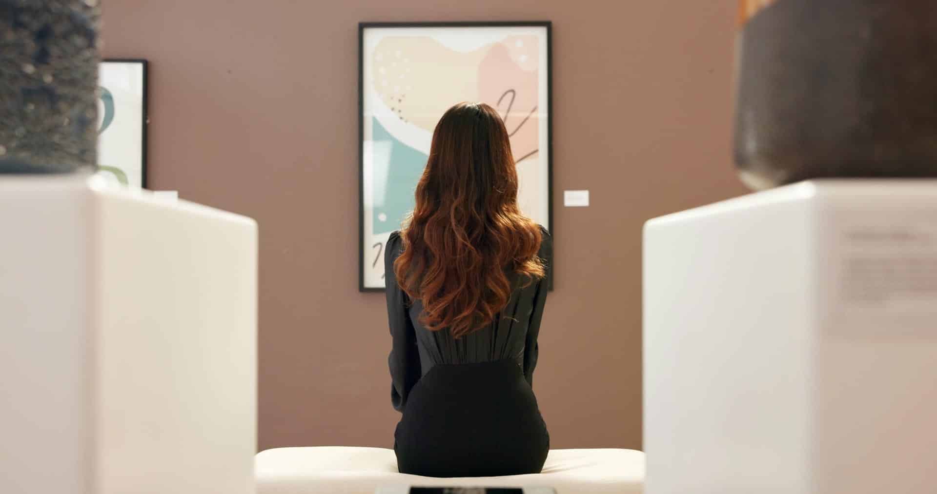 Woman sitting in gallery, admiring artwork on wall.