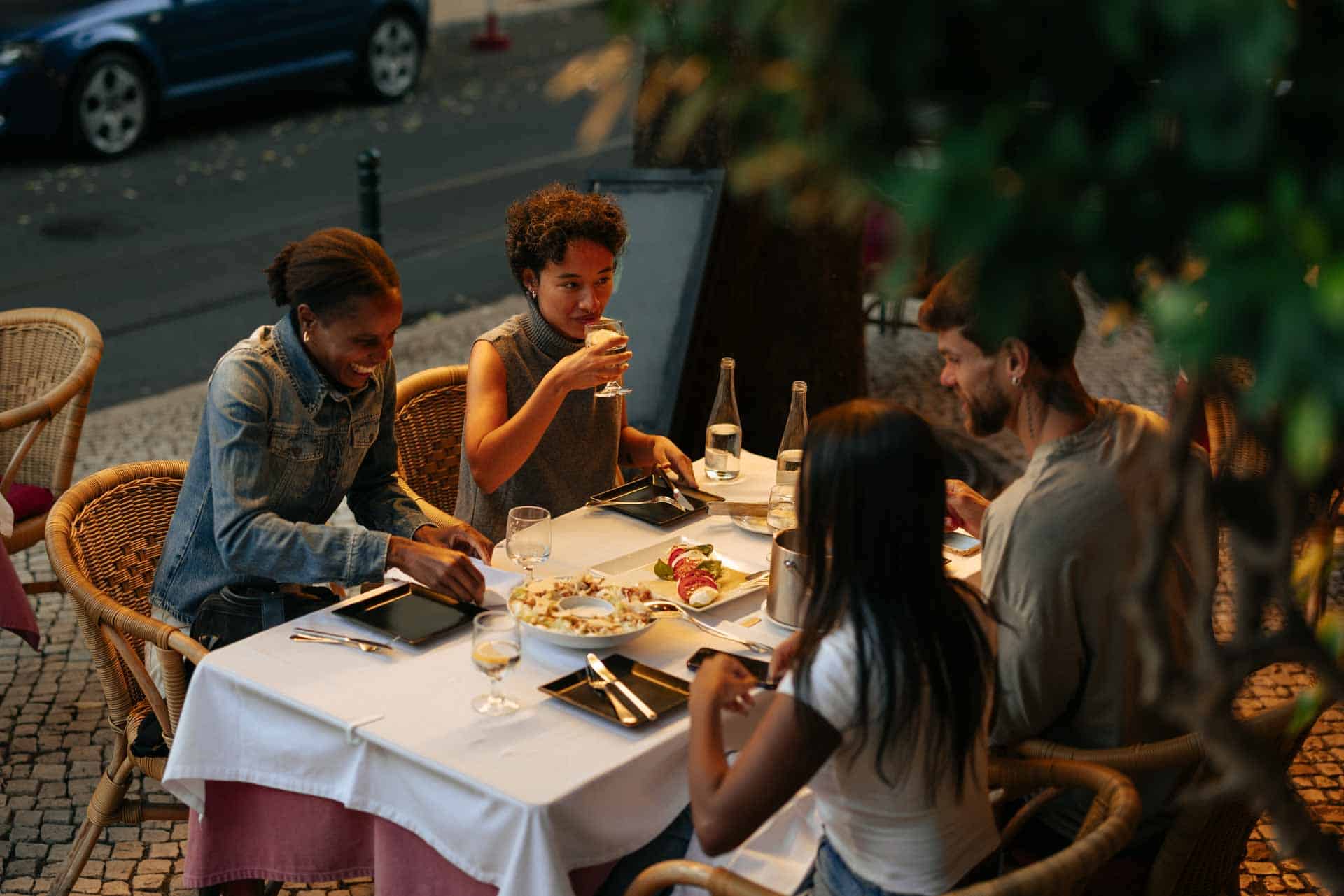 Groupe d'amis dégustant un repas et des boissons dans un restaurant en plein air, célébrant l'amitié et les bons moments.