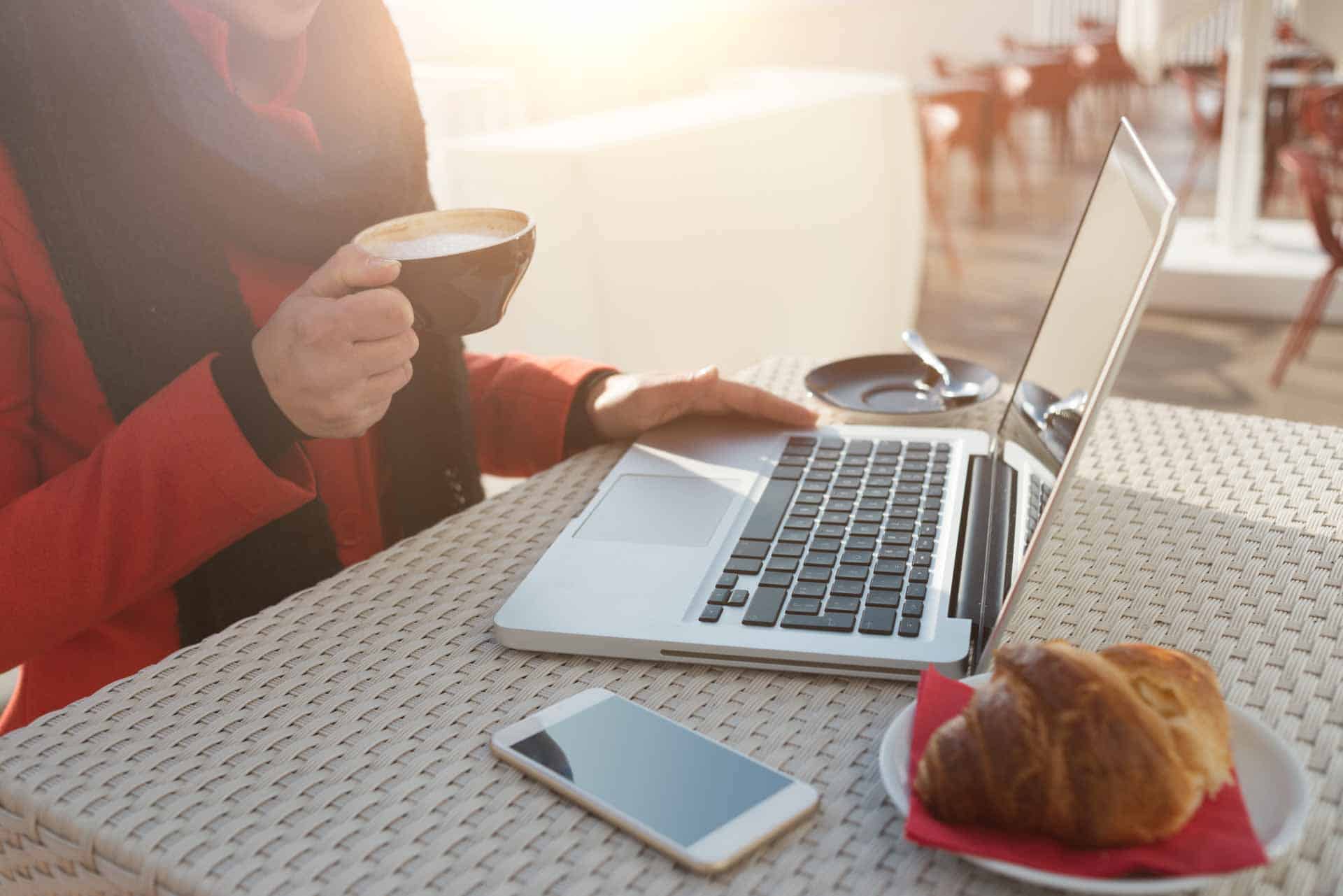 Young woman having breakfast on a cafe terrace and working on her computer