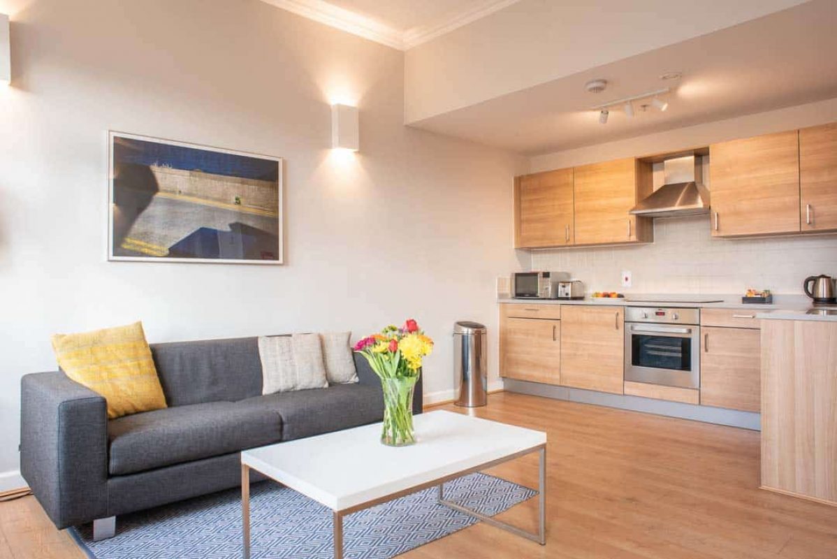 Open plan space to relax with sofa, leading to kitchen at PREMIER SUITES PLUS Glasgow George Square
